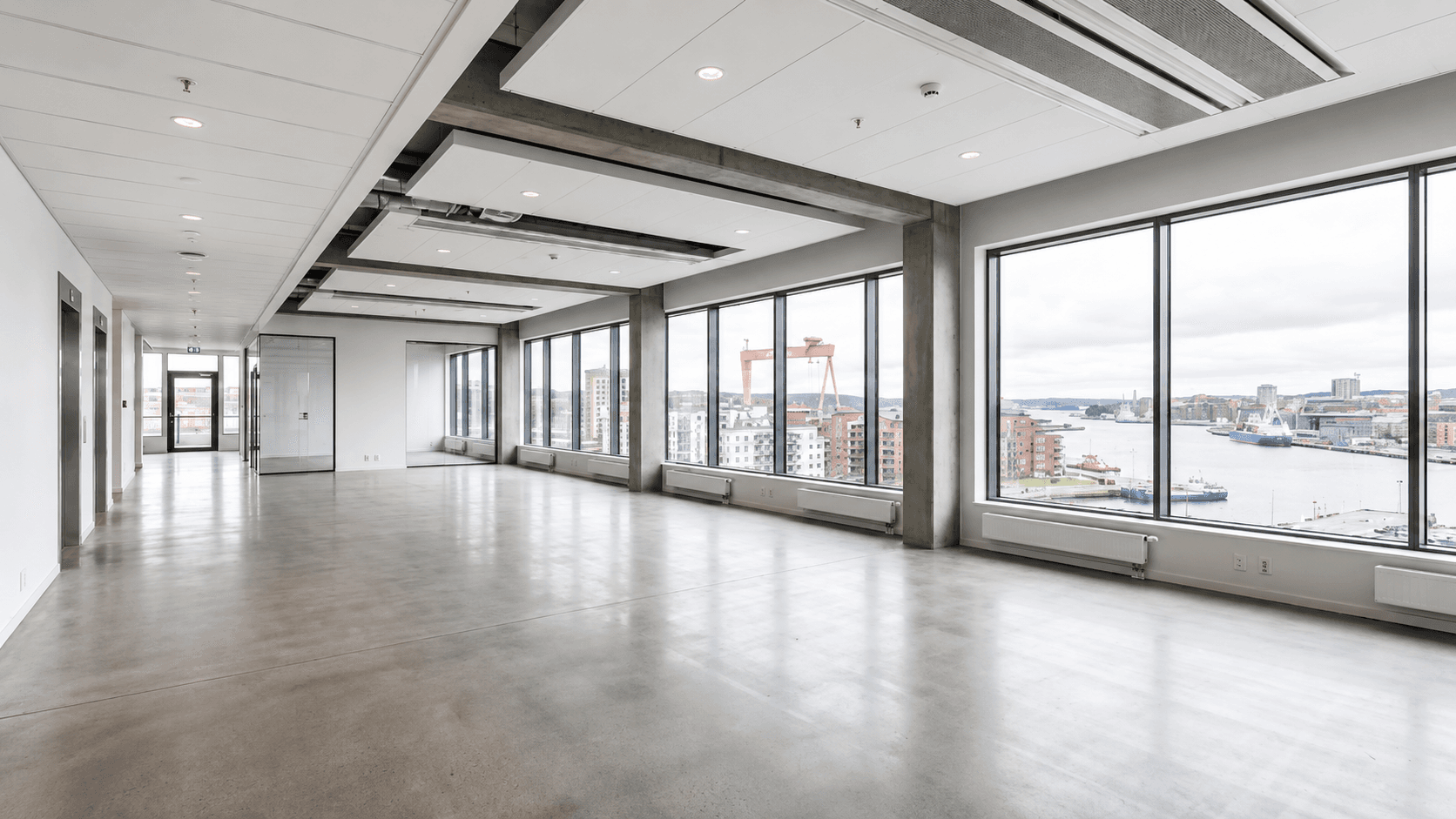 Empty office floor on an upper level with concrete columns and floor-to-ceiling windows looking onto a harbor